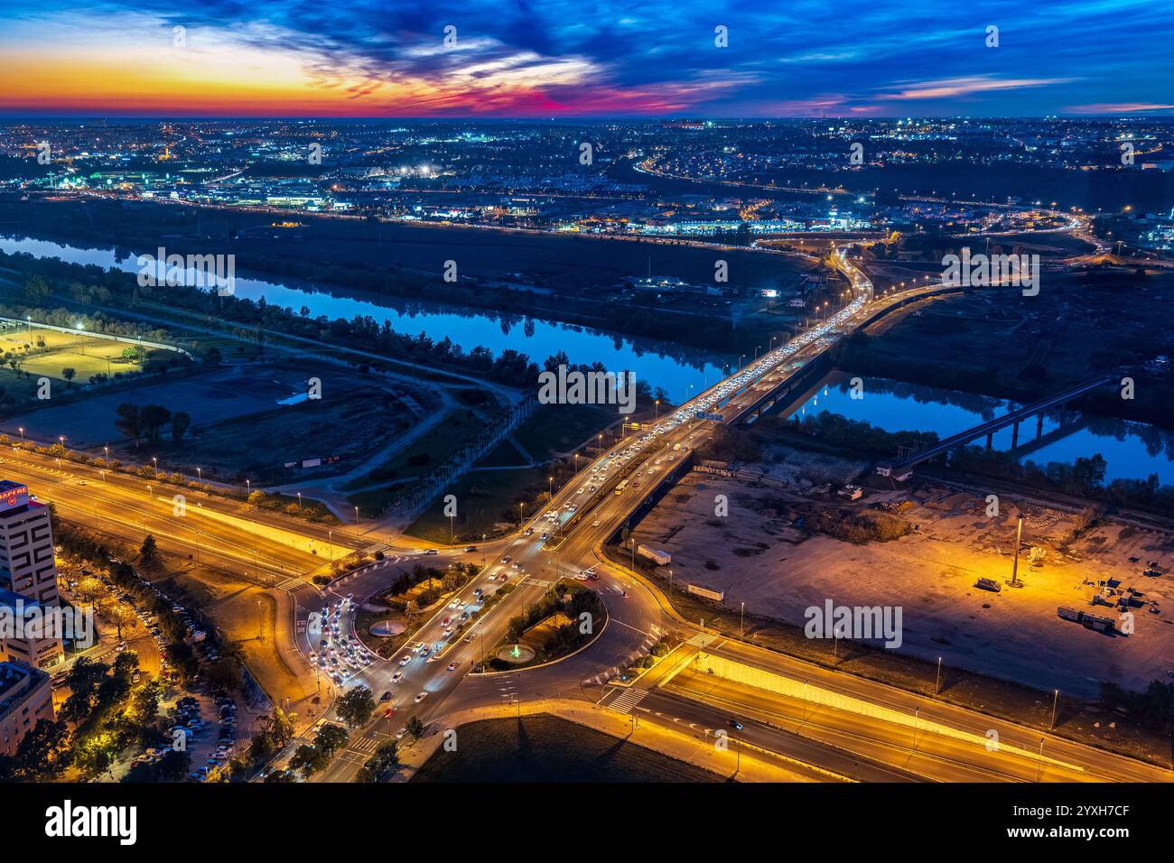 Die Autobahn A49 verbindet Sevilla mit Huelva und überquert bei Sonnenuntergang den Fluss Guadalquivir. Der Verkehr fließt reibungslos unter einem bunten Himmel. Stockfoto