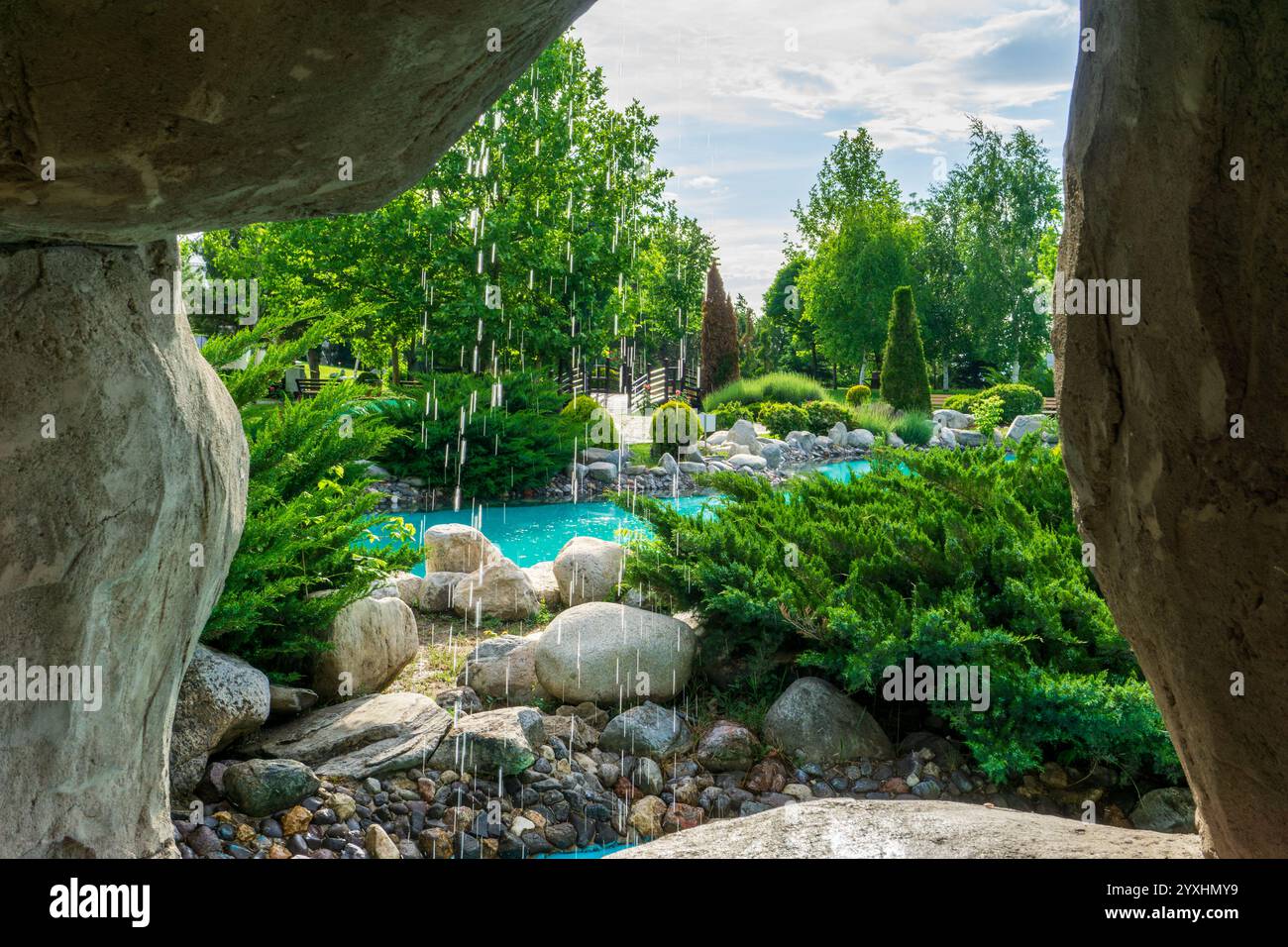 Gartenszene eingerahmt von Stein und fallendem Wasser. Eine wunderschöne Gartenoase hinter einem Steinwasserfall Stockfoto