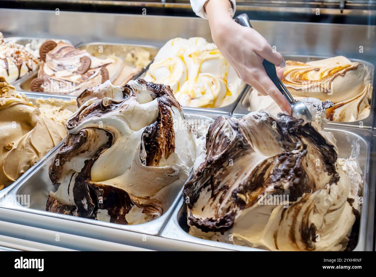 Cremiges Vanille- und Schokoladeneis, serviert mit einem Löffel aus einer Vitrine mit mehreren Geschmacksrichtungen in einem Dessertgeschäft, einem Foodtruck-Eisstadion Stockfoto
