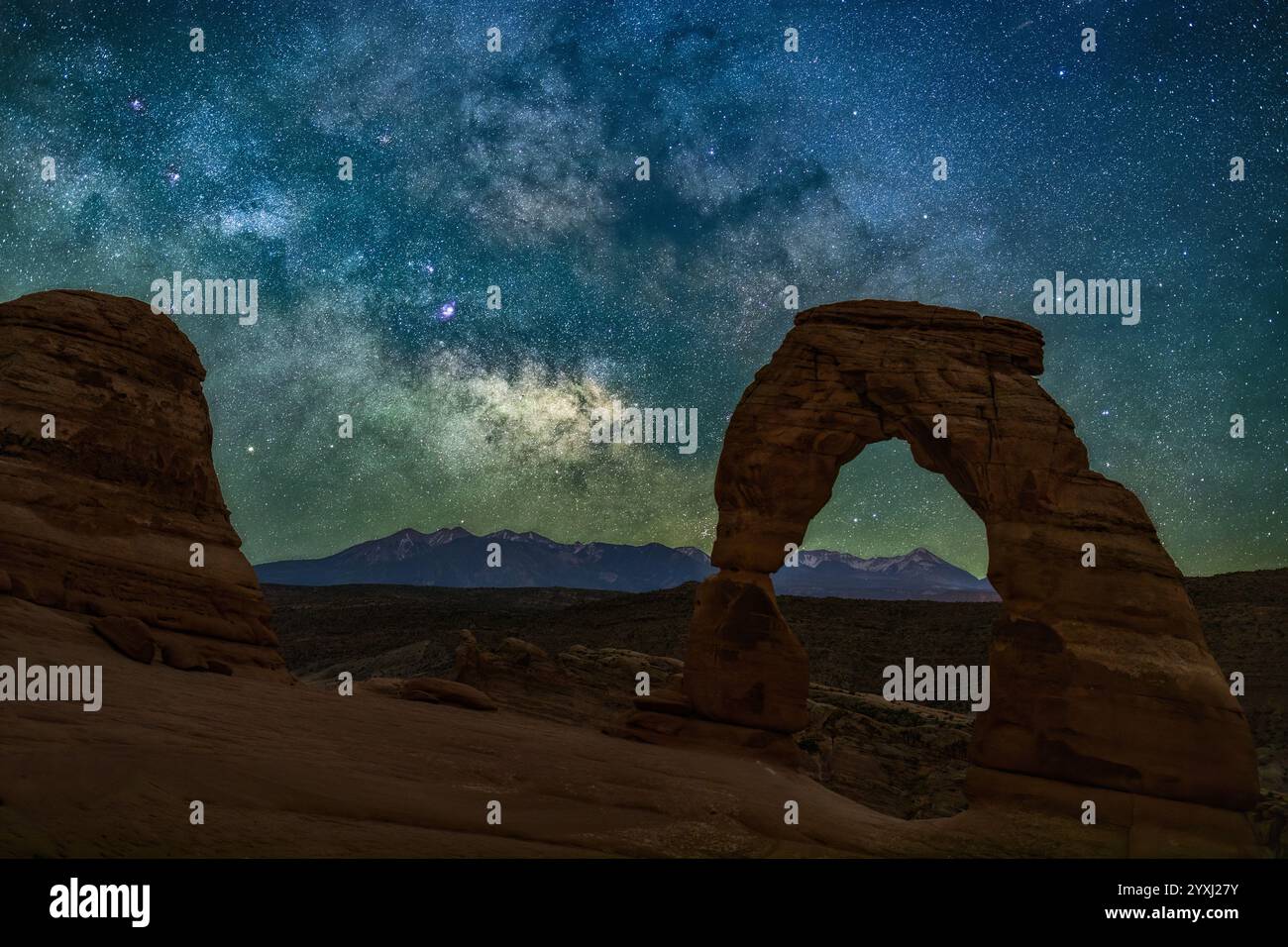 Hinter Delicate Arch erhebt sich eine brillante, farbenfrohe Milchstraße über den La Sal Mountains im Arches National Park, Utah. Stockfoto