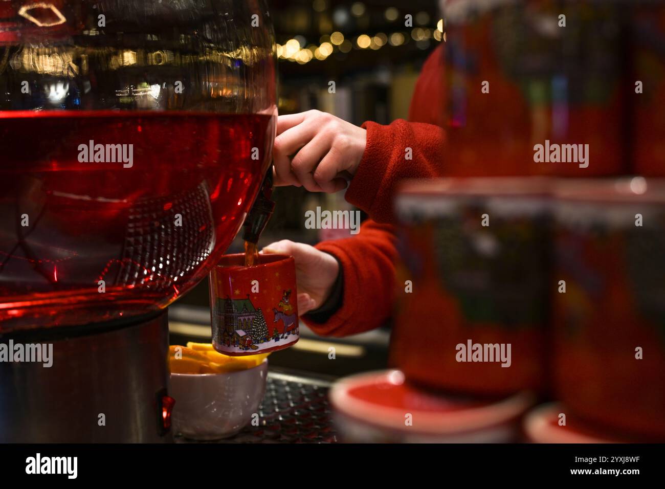 Hände einer Frau in einem roten Pullover, die auf dem Weihnachtsmarkt roten Glühwein in einen Keramikbecher klopft, typisches saisonales Heißgetränk in Deutschland, Copy Spac Stockfoto