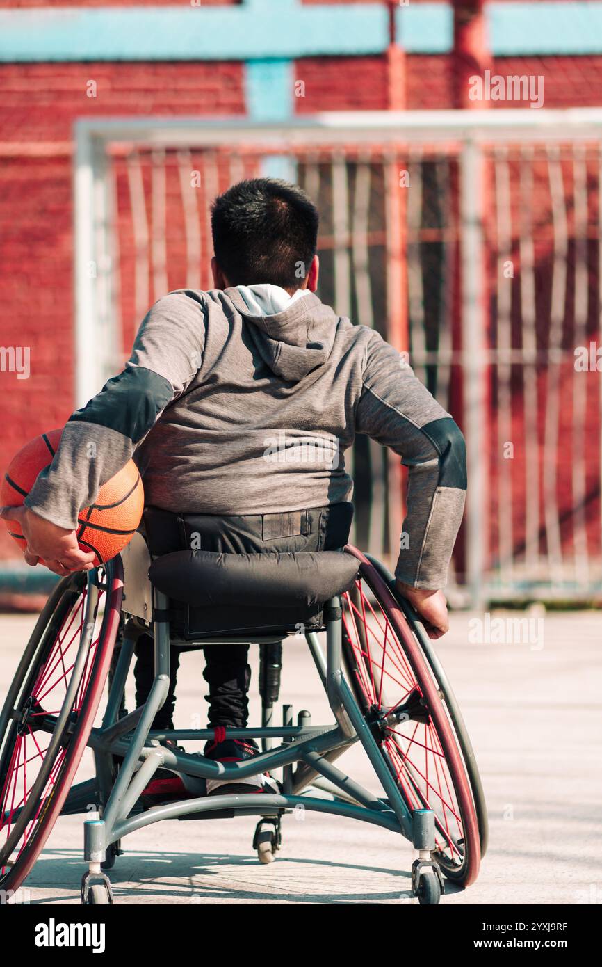 Junger Latino-Athlet im Rollstuhl, Training, Spiel und Konzentration mit Basketball in einem Stadtpark im Freien Stockfoto