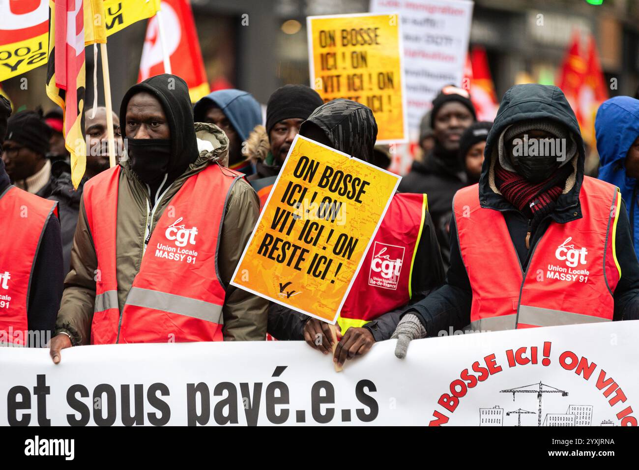 Paris, Frankreich. Dezember 2024. Ein Demonstrant hält während der Demonstration zur Unterstützung der nicht dokumentierten Migranten ein Plakat mit der Aufschrift „Wir arbeiten hier, wir leben hier, wir bleiben hier“. Hunderte von Menschen demonstrierten in Paris gegen die französische Migrationspolitik. Mehrere Gewerkschaften und Verbände haben sich der Aktion angeschlossen, um Migranten ohne Papiere sowie diejenigen zu unterstützen, die regularisiert sind, aber gleichermaßen von der französischen Bürokratie betroffen sind. Quelle: SOPA Images Limited/Alamy Live News Stockfoto