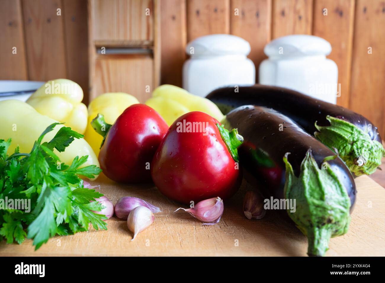 Eine Vielzahl von frischem Gemüse, einschließlich Paprika, Auberginen und Knoblauch, ist auf einem Schneidebrett in einer warmen, rustikalen Küche, Showcasin, ordentlich angeordnet Stockfoto