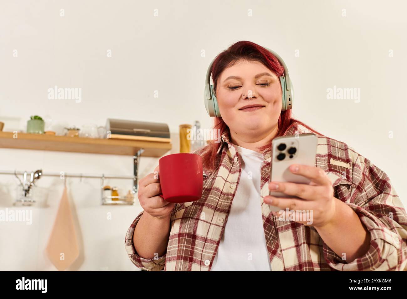 Eine junge Frau in Übergröße genießt einen friedlichen Moment mit ihrem Getränk, während sie Musik hört. Stockfoto