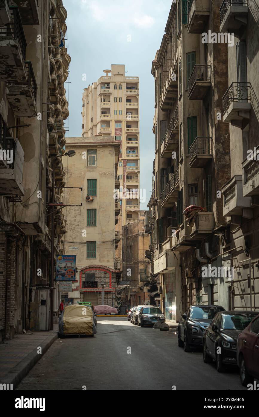 Eine enge, stimmungsvolle Straße in Alexandria, Ägypten, mit alten historischen Gebäuden mit Balkonen, modernen Hochhäusern und geparkten Autos. Stockfoto