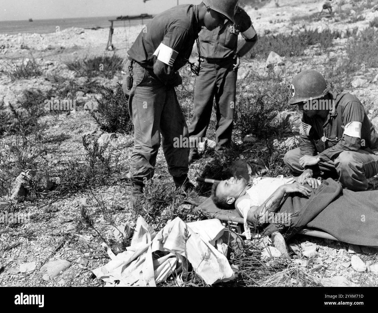 7. Armee amerikanische Sanitäter, die einen am D-Day (6. Juni) verwundeten Soldaten betreuen, der auf einem Wurf auf dem Strandkopf lag, 17. August 1944 Stockfoto