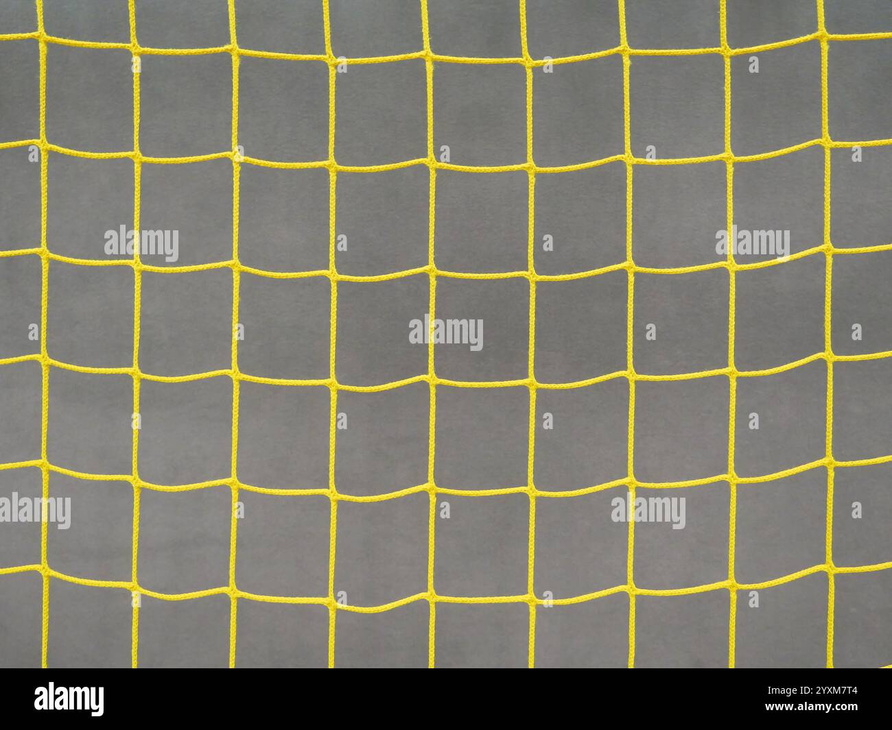 Nahaufnahme des gelben Fußballtornetzes: Geometrisches Netz gegen graue Schutzwand in einer Sporthalle mit Retro-Charme. Stockfoto