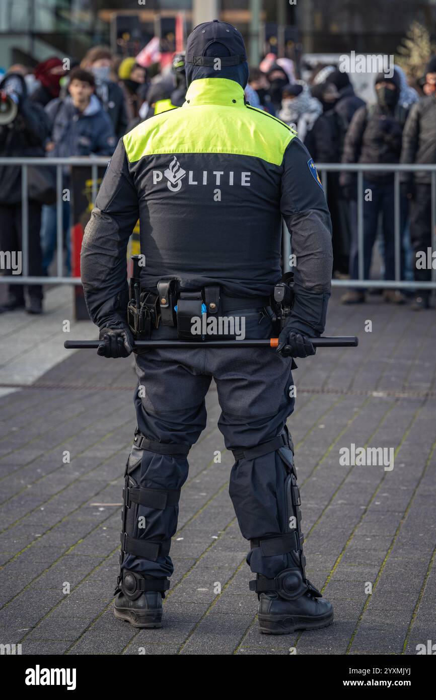 Rotterdam, Niederlande, 21.11.2024, niederländischer Polizeibeamter, der Demonstranten gegenübersteht und bei einer Protestkundgebung einen Baton hinter seinem Rücken hält, Rückansicht Stockfoto