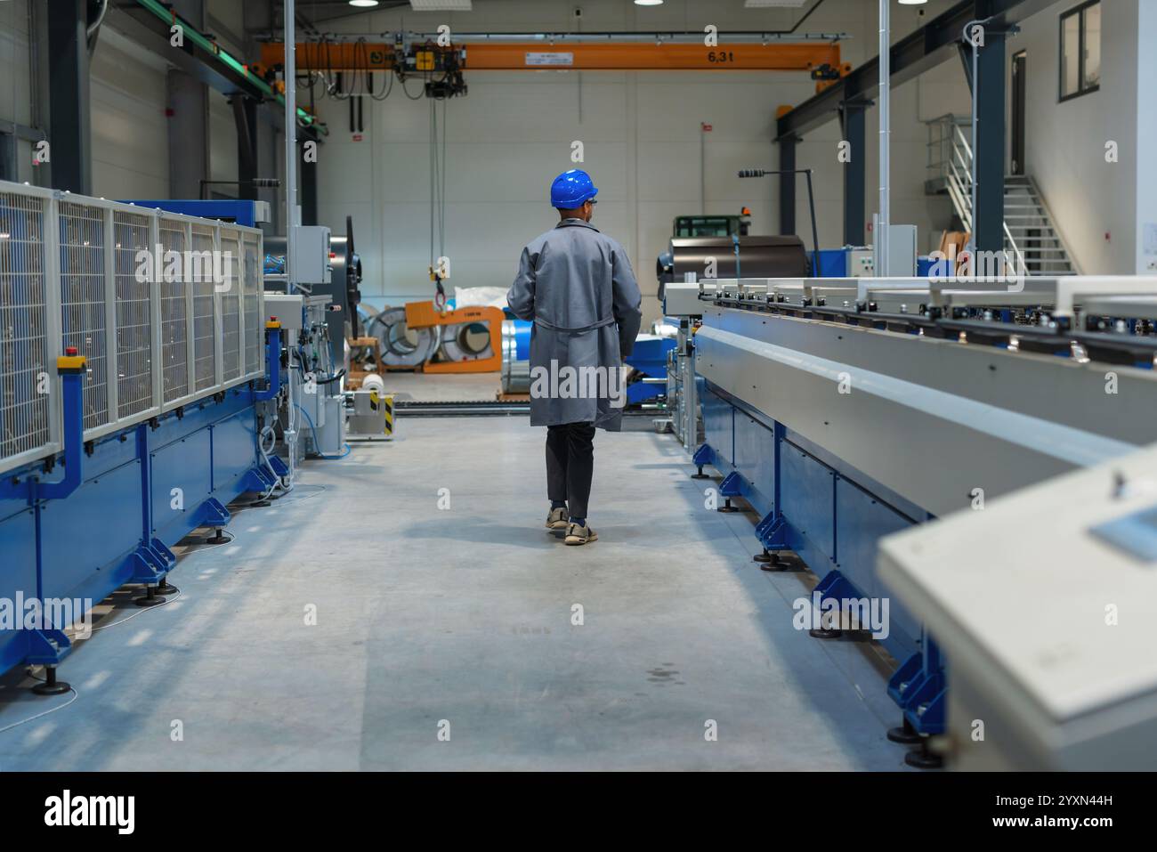Afroamerikanischer Ingenieur, der einen grauen Arbeitsmantel und einen blauen Helm trägt und die Produktion und Programmierung einer Maschine in einer Fabrik steuert. Stockfoto