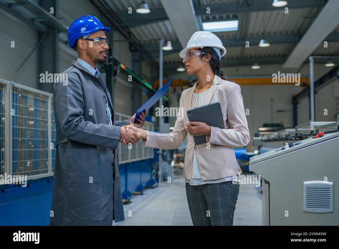 Indische Managerin und afroamerikanischer Chefingenieur gehen durch die Fabrik, sprechen und planen Produktionsoptimierung, Vorderansicht. Stockfoto