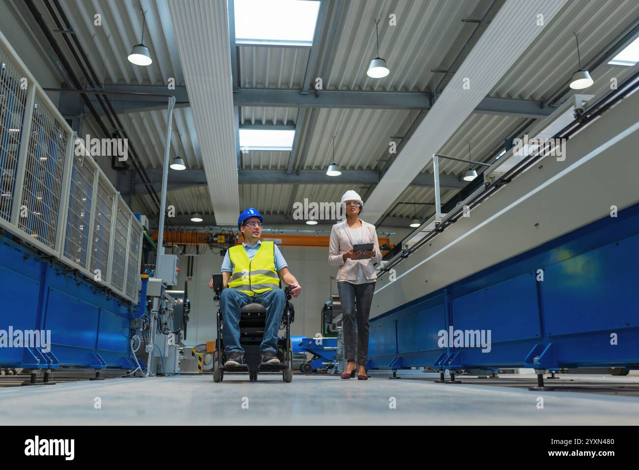 Weibliche Führungskraft, die einen neuen Mitarbeiter mit einer Behinderung für einen Job ausbildet, erklärt die Arbeit an Maschinen. Industrie, Integration und Arbeitsplatzkonzept. Stockfoto