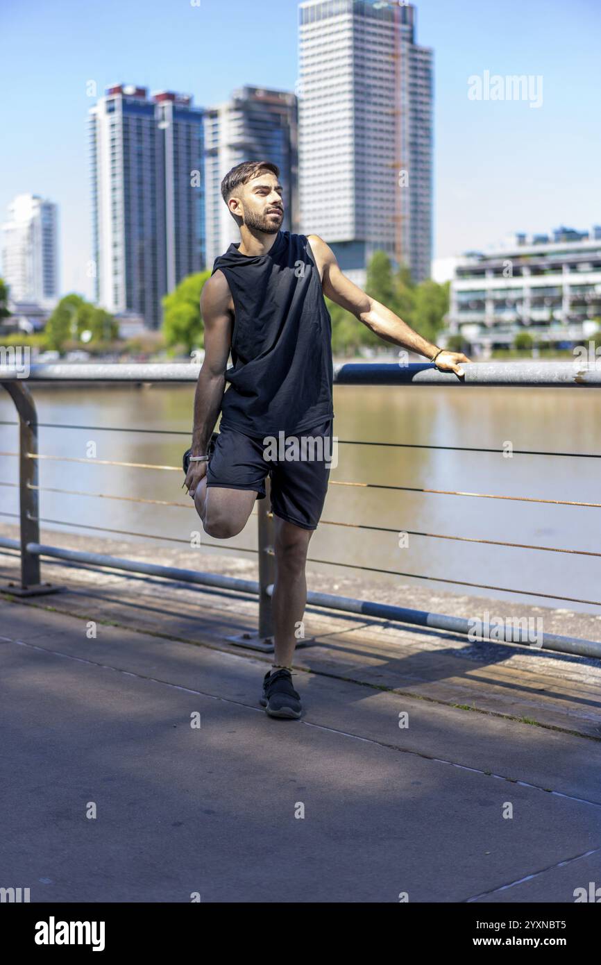 Fitter junger Mann, der an Flexibilitätsübungen entlang eines Stadtkanals teilnimmt. Stockfoto