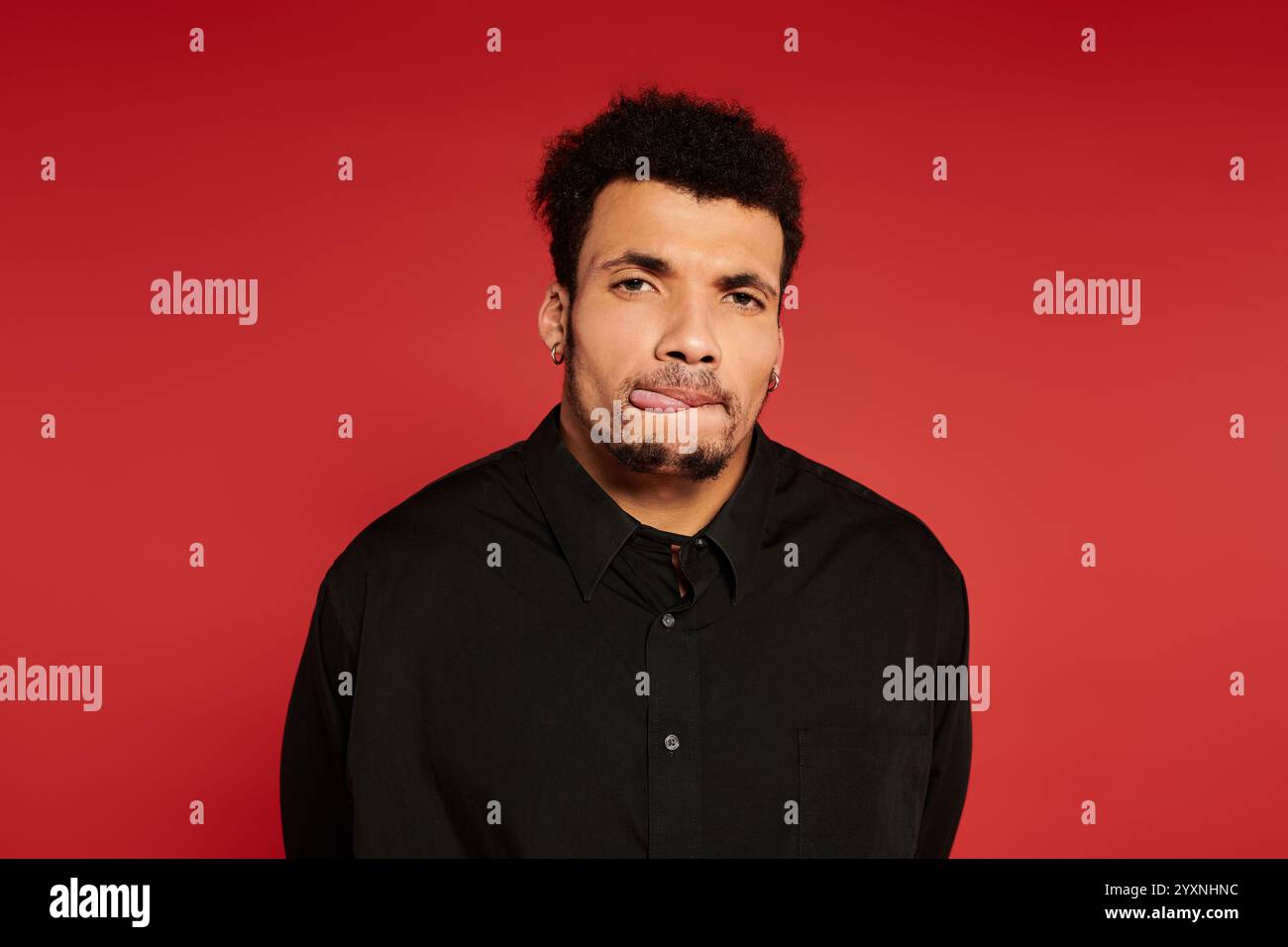 Ein junger, gutaussehender Mann steht mit einem leichten Lächeln vor einem leuchtend roten Hintergrund. Stockfoto