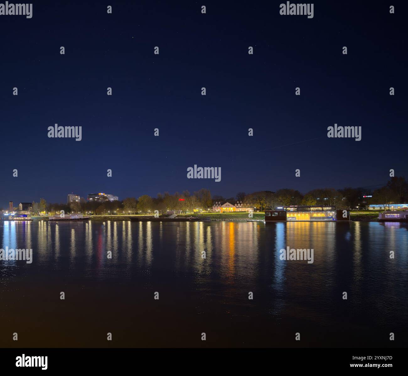 Nächtlicher Blick auf ein Flussufer der Stadt mit farbenfrohen Lichtern, die auf der ruhigen Wasseroberfläche reflektieren und eine ruhige und malerische Szene schaffen. Stockfoto