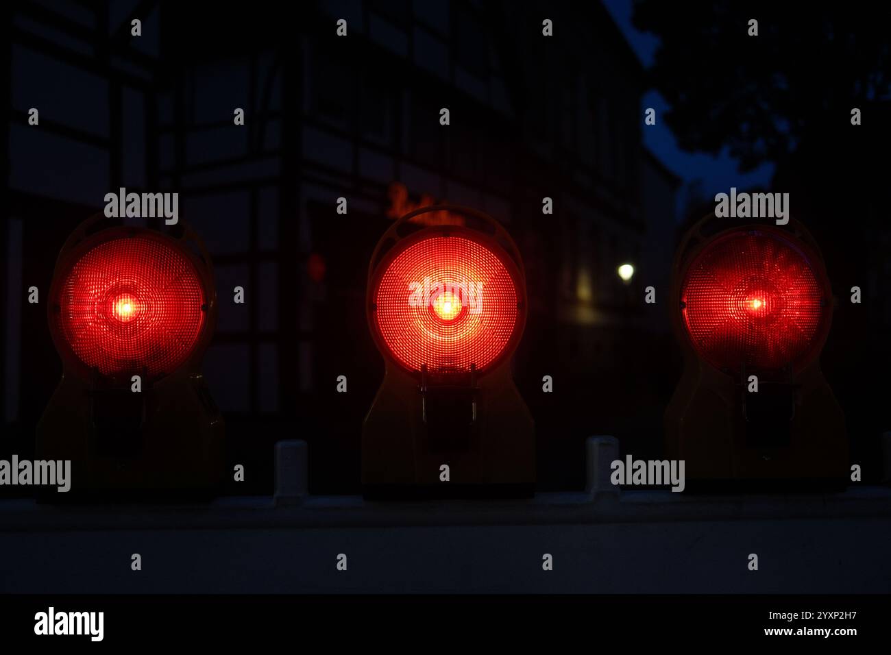 Im Dunkeln leuchten drei rote Lichter auf. Die Lichter sind auf einem Zaun Stockfoto