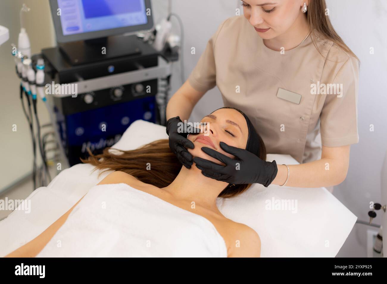 Eine Frau genießt eine friedliche Gesichtsbehandlung in einer ruhigen Spa-Umgebung, umgeben von beruhigenden Farben und sanften Händen, die ein revitalisierendes Erlebnis bieten Stockfoto