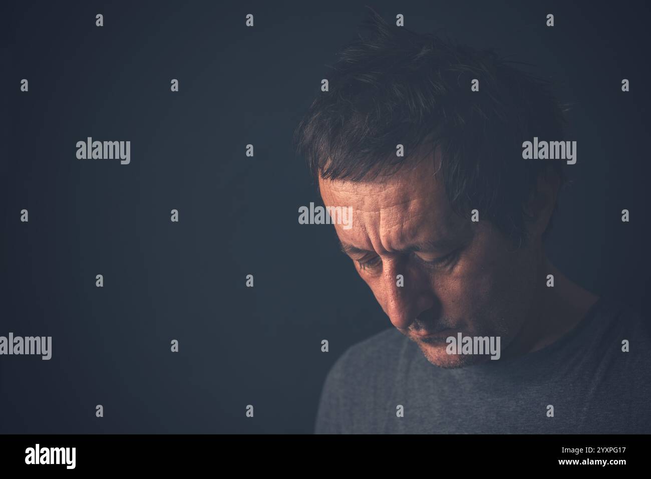 Unglücklicher besinnlicher erwachsener Mann, der in Dunkelkammer denkt, depressiv schmollende männliche Gedanken, selektiver Fokus Stockfoto