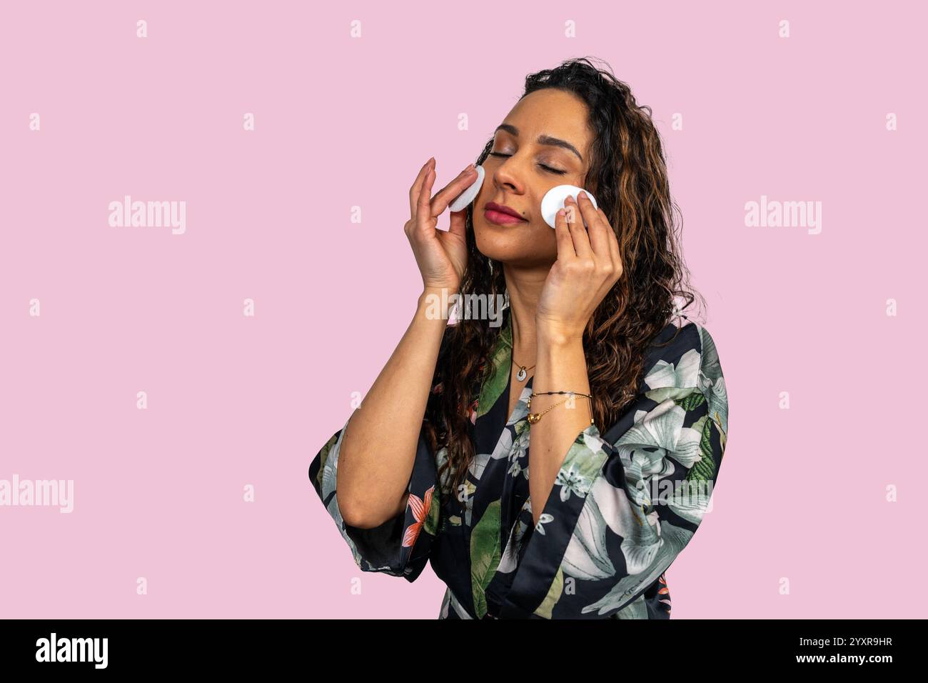 Lateinische Frau entfernt sanft Make-up mit Wattepads und genießt ihre Hautpflegeroutine Stockfoto