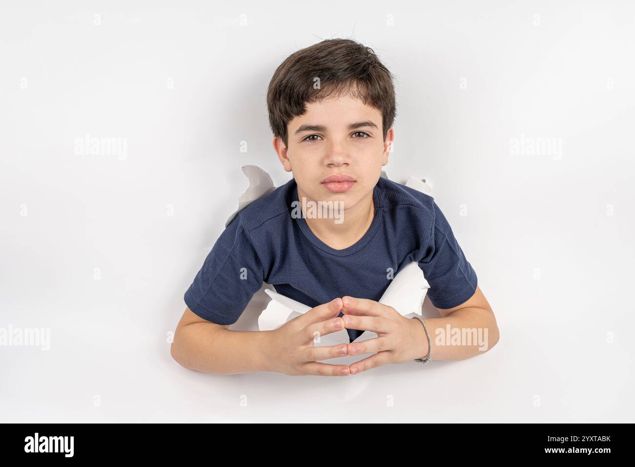 11-jähriges brasilianisches Kind mit seinem Körper durch einen weißen Karton, der seine Fingerspitzen berührt. Stockfoto