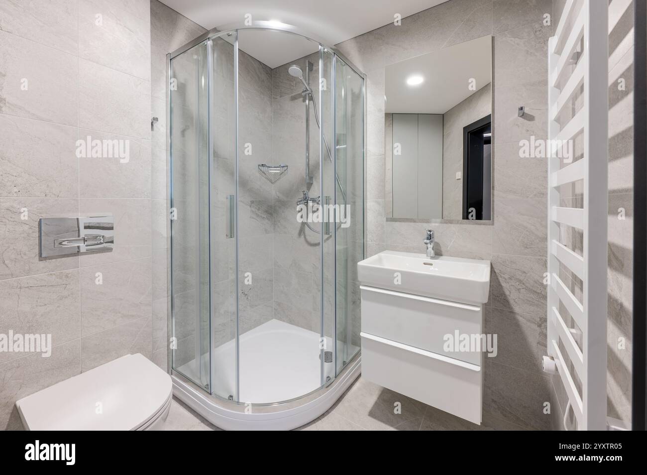 Modernes Bad mit verglaster Dusche, elegantem weißem Waschbecken, grauen gefliesten Wänden und modernen Annehmlichkeiten in einem ordentlichen und minimalistischen Ambiente Stockfoto