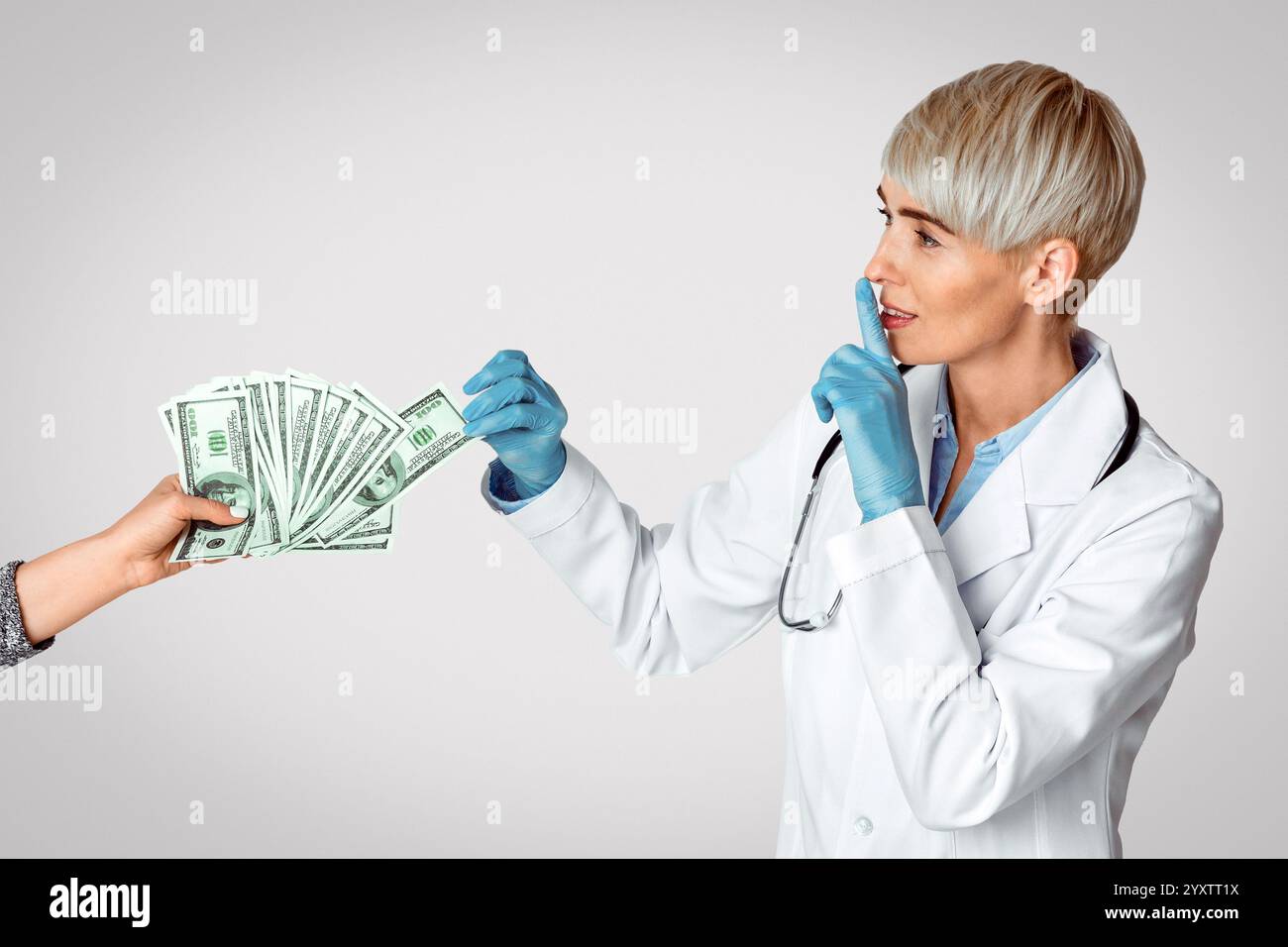 Frau Ärztin in medizinischen Handschuhen nimmt Geld von den Händen des Patienten und macht Zeichen der Stille Stockfoto