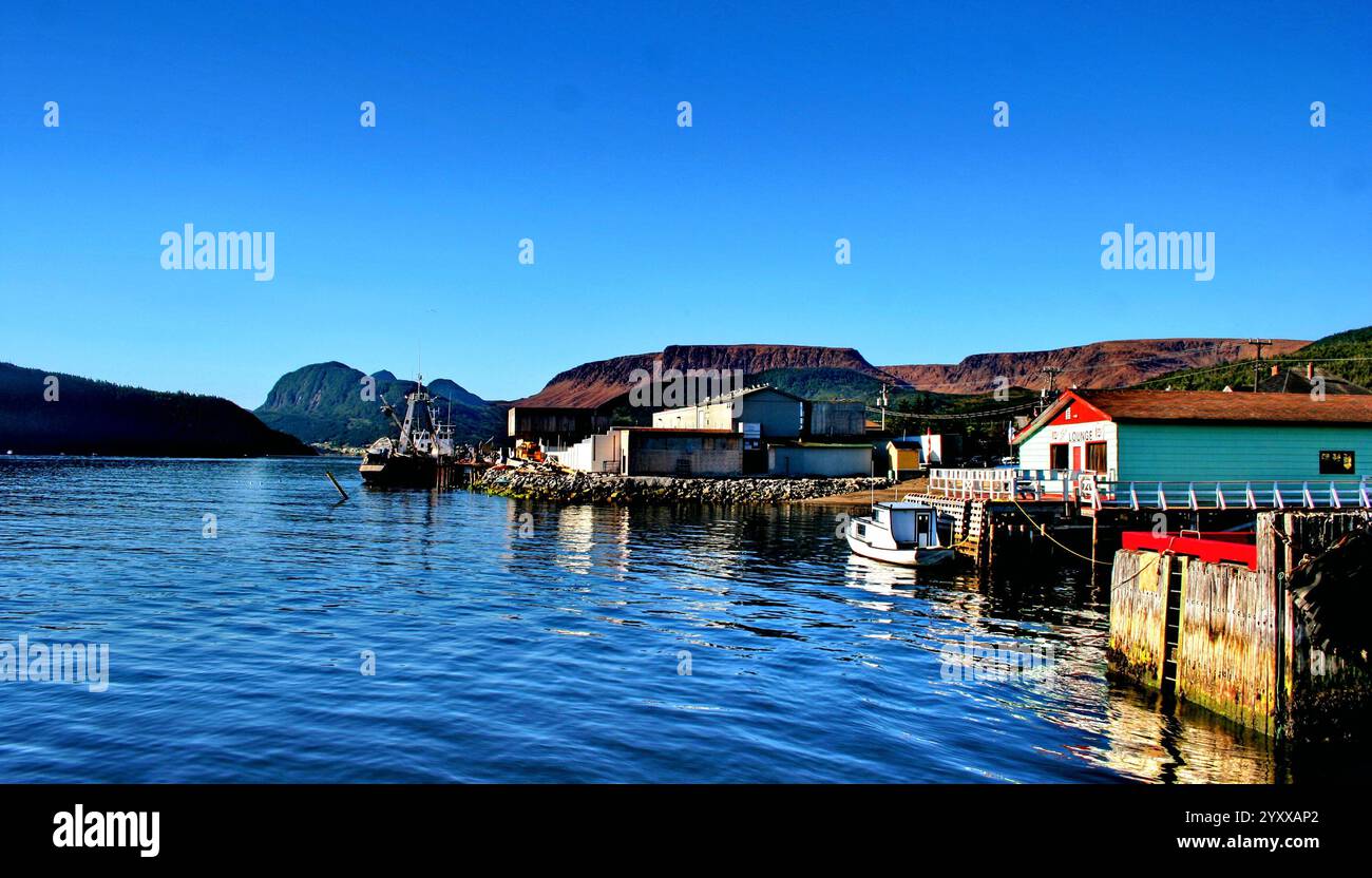 Eine malerische Küstenszene in Neufundland, Kanada, mit einem kleinen Boot, das von einer farbenfrohen Lounge mit bergigem Hintergrund angedockt wird. Stockfoto