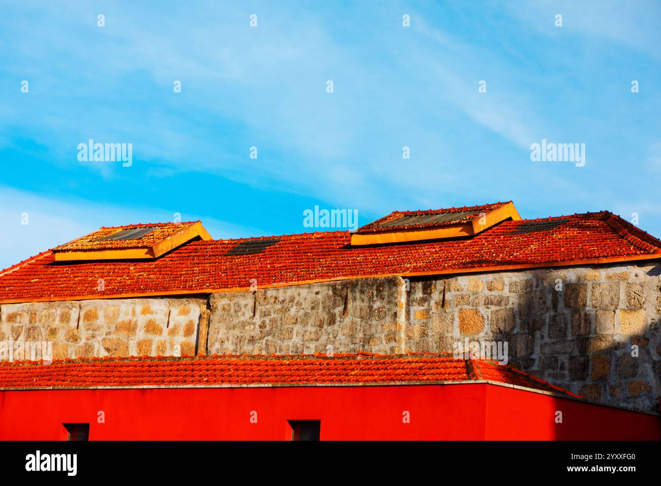 Gebäude mit einem leuchtend roten unteren Abschnitt und einem oberen Abschnitt aus Stein, gekrönt von einem rot gekachelten Dach. Das Dach verfügt über Dachfenster und den Himmel im bac Stockfoto