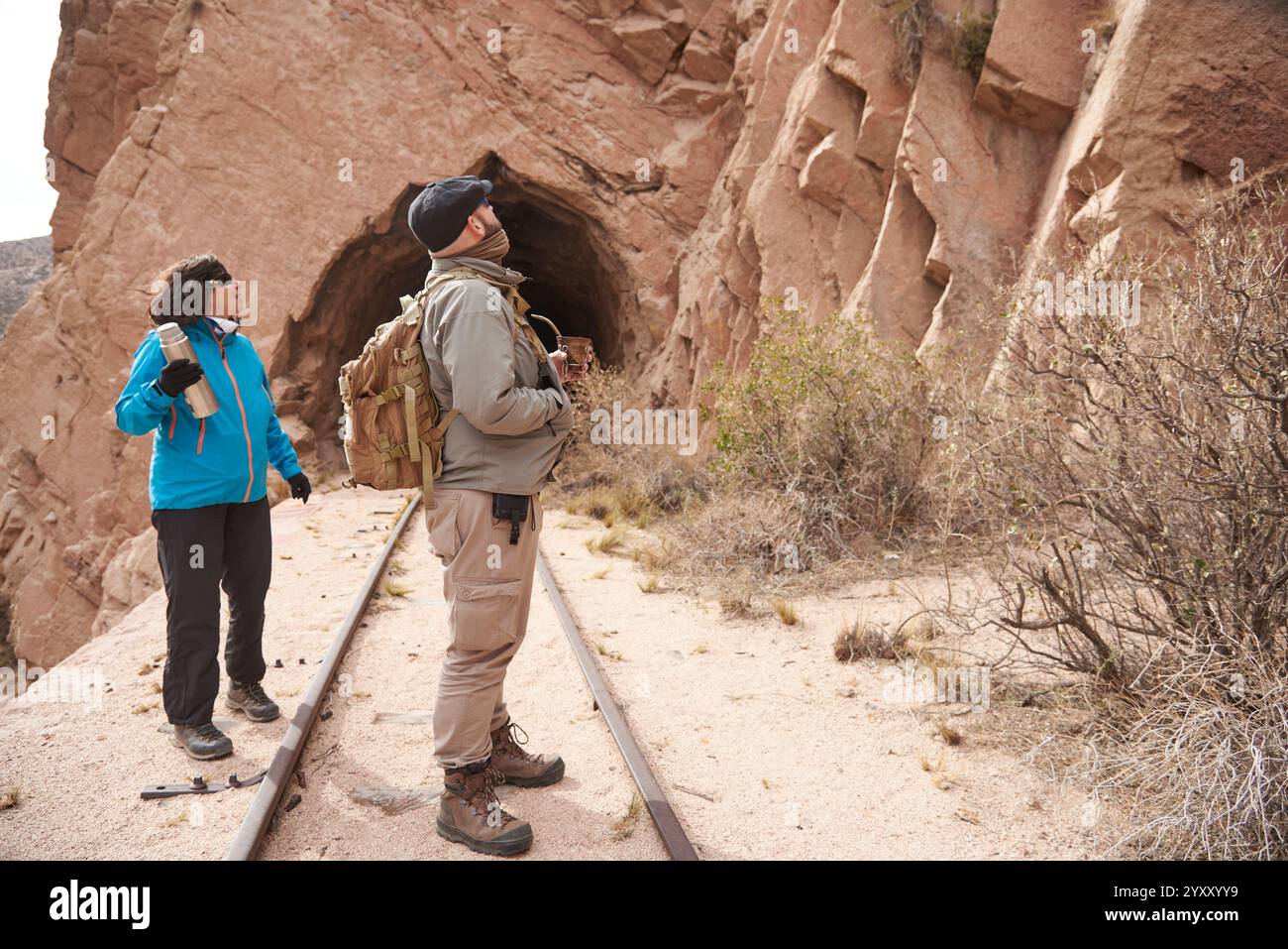 Ein paar Reisende Freunde, Mann und Frau, die die Gleise entlang laufen. Im Hintergrund befindet sich ein Tunnel. Beide schauen nach oben und sehen etwas an Stockfoto