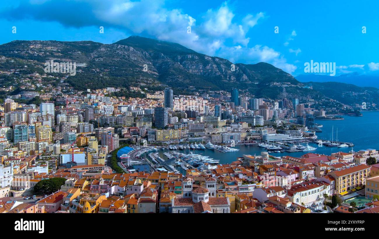 Atemberaubende Luftaufnahme von Monacos pulsierendem Hafen, luxuriösen Yachten, farbenfrohen Gebäuden und dramatischer Bergkulisse. Ideal für Reisen und Luxusleben Stockfoto