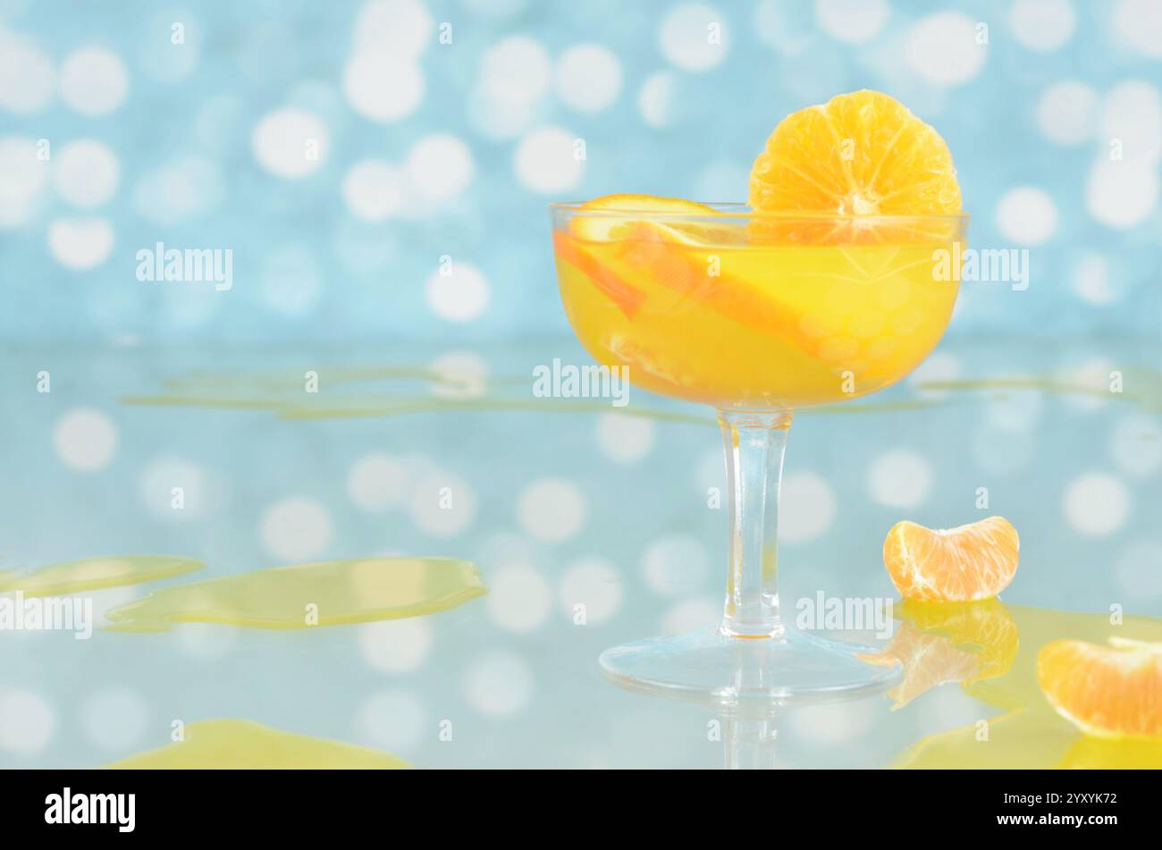 Orangencocktail mit Zitrusfrüchten im Glas, verschütteter Saft, Mandarine, Glastisch mit Reflexionen und leerer Raum zum Füllen mit Inhalt. Stockfoto