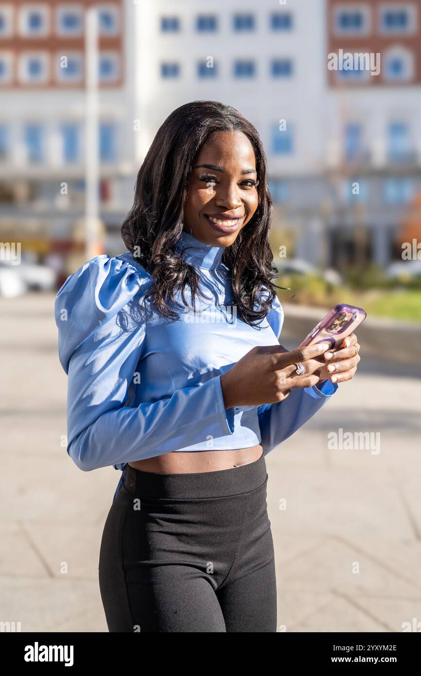 Junger Manager lächelt und nutzt ein Smartphone in einer städtischen Umgebung Stockfoto