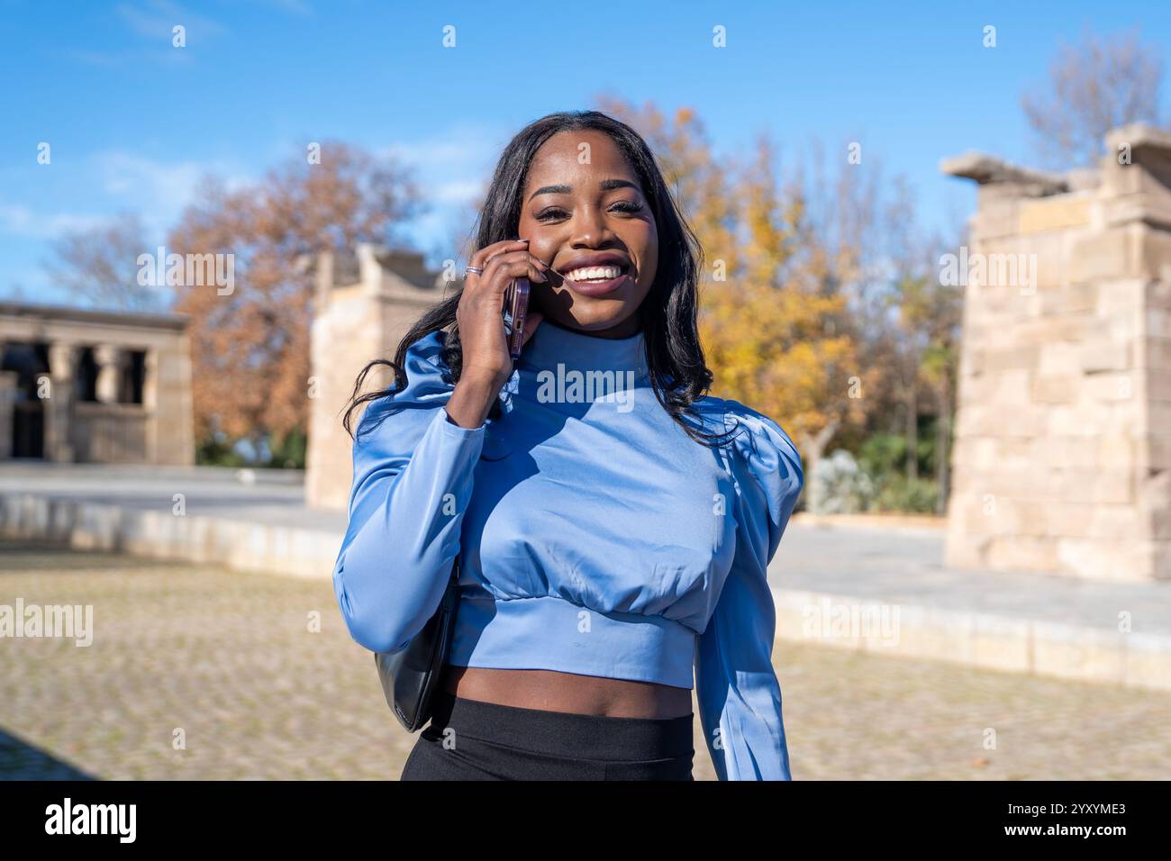 Junge schwarze Geschäftsfrau, die ihr Smartphone im debod-Tempel in madrid am sonnigen Tag benutzt Stockfoto