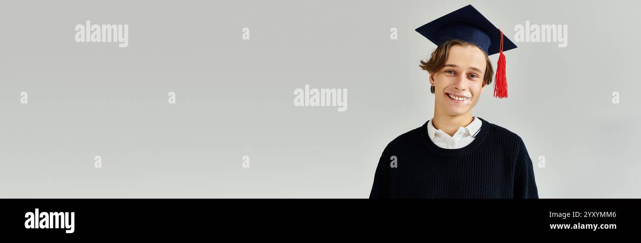Ein junger Mann, der eine Abschlussmütze trägt, lächelt stolz in einem Studio während seiner College-Jahre, Banner Stockfoto
