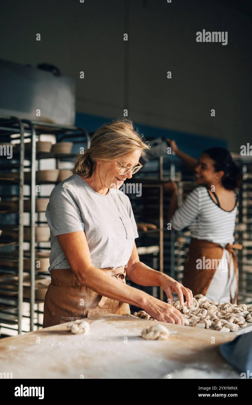 Lächelnde ältere Bäckerin, die Zimtbrötchen auf einem Tablett arrangiert, während sie in der Bäckerei arbeitet Stockfoto