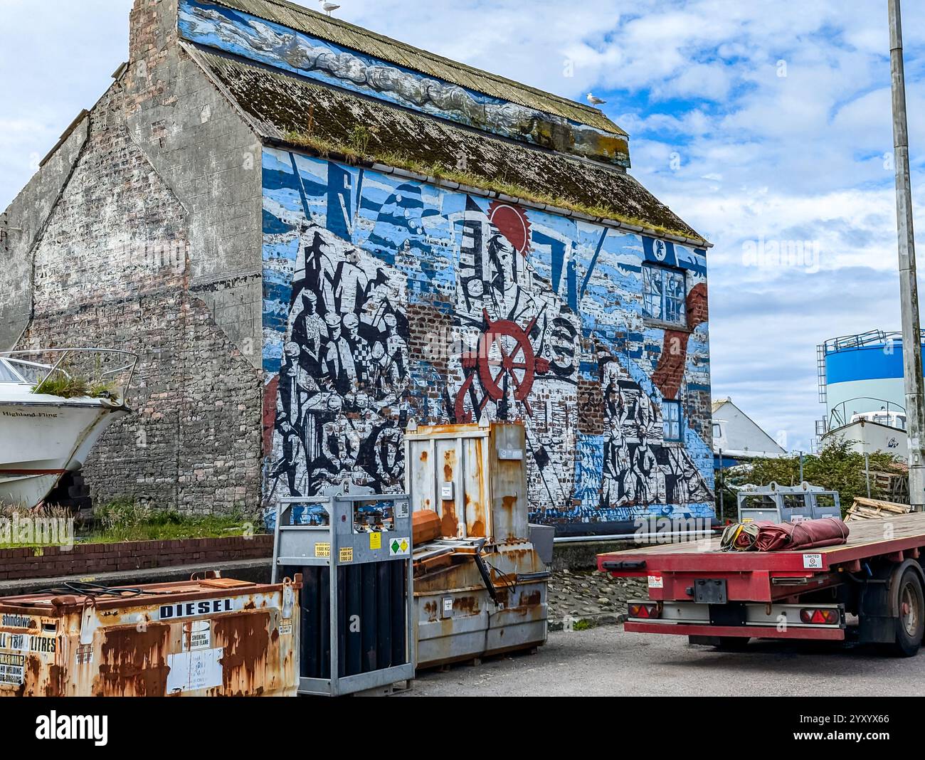 Industriegebäude am Wasser mit maritimen Wandgemälden, Boot, Tieflader und Containern. Mallaig, Schottland Stockfoto