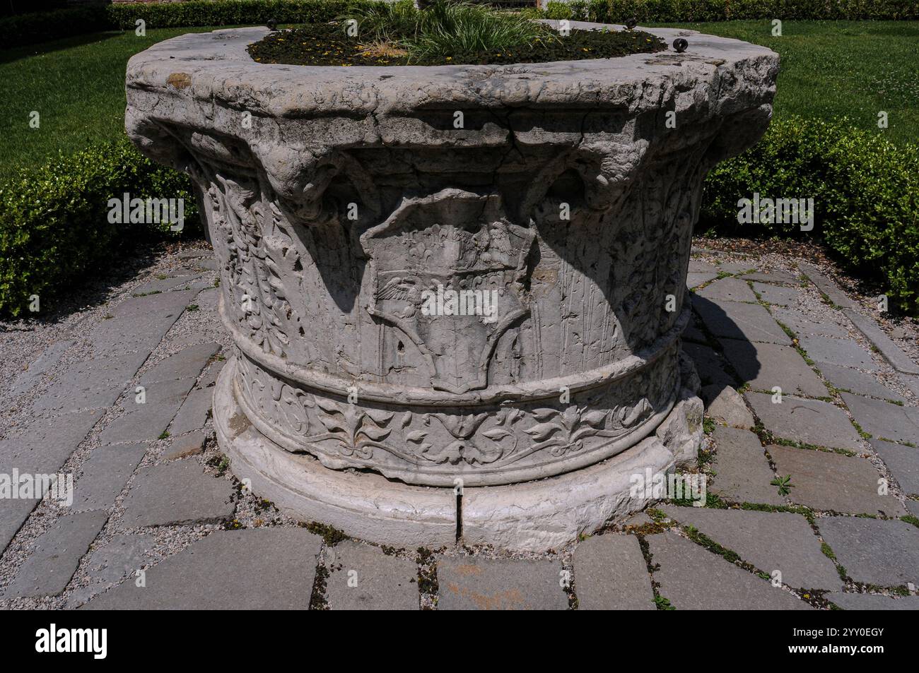 Brunnenkopf mit einem geviertelten Wappenschild im Garten des Palazzo dei Diamanti, einem Renaissance-Palast in Ferrara, Emilia-Romagna, Italien. Das Wappenschild enthält einen gekrönten Adler, Wappen des Hauses Este. Stockfoto