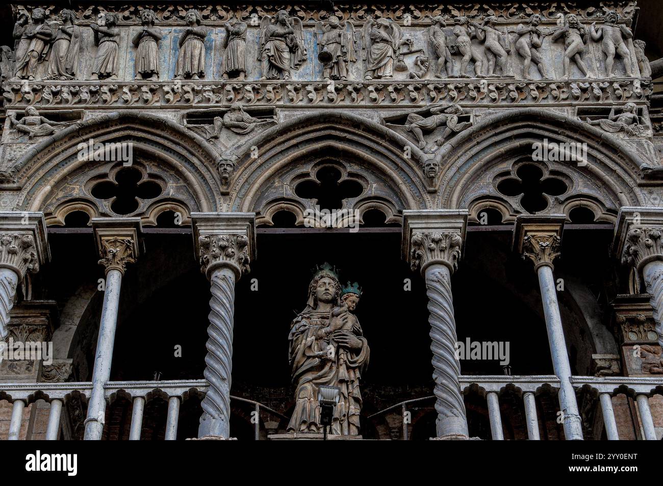 Statue der gekrönten Jungfrau und des Kindes von 1427 von Christoforo da Firenze, Westfront der Kathedrale St. Georg (Duomo di San Giorgio Martyre) in Ferrara, Emilia-Romagna, Italien. Die Statue befindet sich in einer Loggia, die in den 1200er Jahren hinzugefügt wurde und wird von zwei Spiralsäulen der Loggia mit Blätterkapitellen flankiert, die Bögen stützen, die von Vierfachfolien durchbrochen wurden. Auf dem Gipfel der Loggia befinden sich Szenen des letzten Jüngsten Gerichts, die in den 1200er Jahren von einem unbekannten Bildhauer im gotischen Stil gemeißelt wurden; dazu gehören das gerettete Rauschen aus ihren Särgen (über den Bögen) und das am Hals angekettete Verdammte (oben rechts). Stockfoto