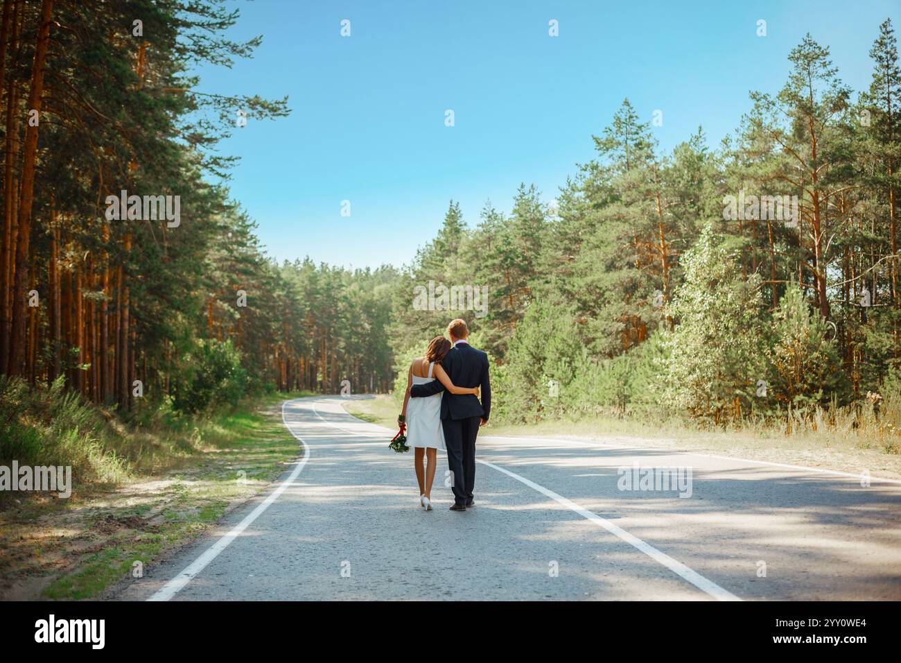 Jungvermählte laufen auf einer Asphaltstraße in einem Kiefernwald. Das Konzept eines langen glücklichen Lebens für zwei Liebende. Stockfoto