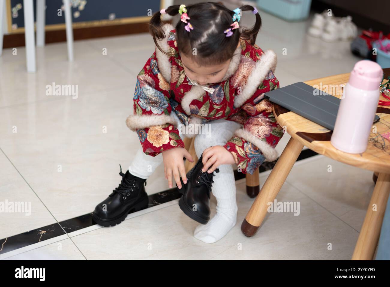 Ein kleines chinesisches Mädchen in traditioneller Tracht zieht Stiefel an. Sie ist bereit, das chinesische Neujahr zu feiern. Stockfoto