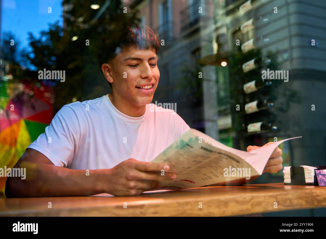 Junger Latino Mann liest Menü im Café mit Stadtreflektionen auf Glas junger Latino Mann liest Menü im Café mit Stadtreflektionen auf Glas Stockfoto