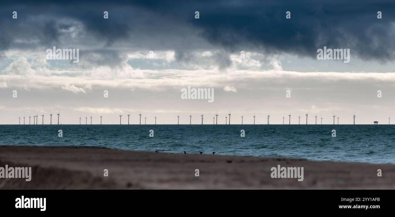 Offshore-Windturbinen erzeugen Elektrizität am Meer dunkler Himmel über dem Panoramablick auf Beton bei gegensätzlichen Lichtverhältnissen im Vordergrund Stockfoto