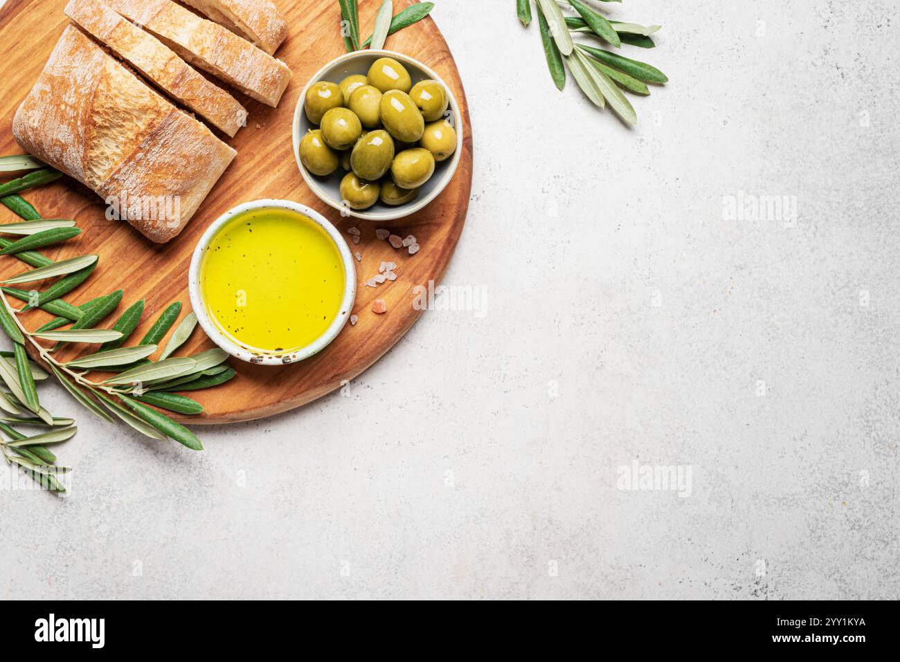 Olivenöl, Oliven und Brot. Bio extra natives Olivenöl in der Schüssel mit grünen Oliven, Blättern und frischem Ciabatta-Brot auf weißem Hintergrund, Draufsicht, Stockfoto