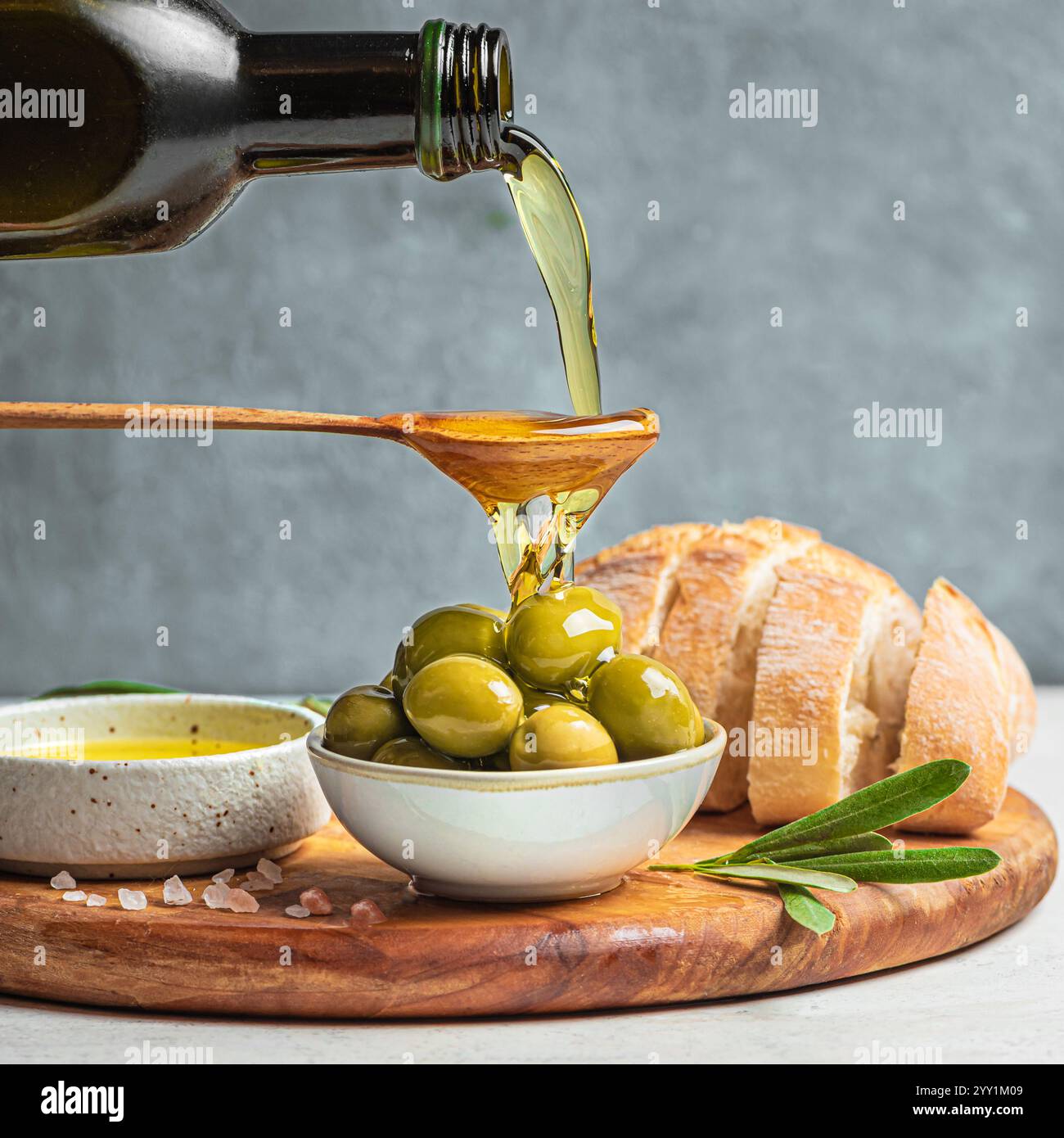 Gießen Sie Olivenöl in einen Löffel über grüne Oliven. Biologisches italienisches kaltgepresstes Olivenöl. Gesundes, mittelgrosses Lebensmittelkonzept. Stockfoto