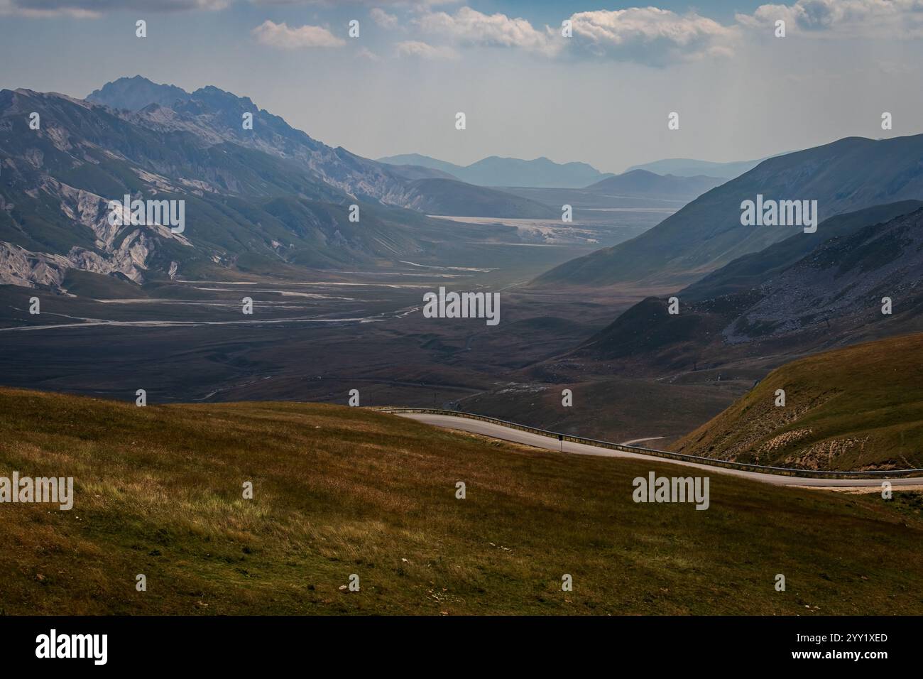 Ausgedehntes Bergtal mit einem dramatischen felsigen Gipfel unter einem hellblauen Himmel und verstreuten Wolken eine atemberaubende, unberührte Naturszene. Stockfoto