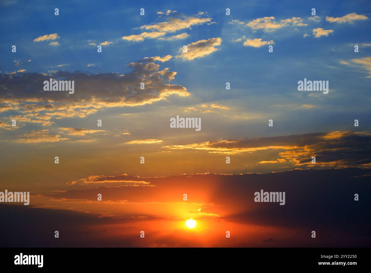 Dramatischer Sonnenuntergang Hintergrund mit heller Sonne, blauem Himmel und malerischen Wolken. Stockfoto
