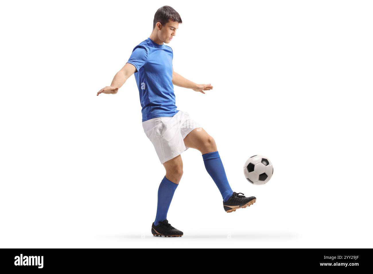 Fußballspieler in einem blauen Oberteil und weißen Shorts, der einen Ball isoliert auf weißem Hintergrund tritt Stockfoto