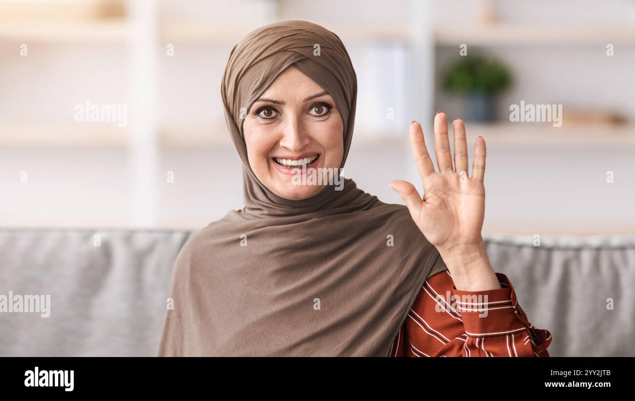 Porträt Einer Älteren Muslimischen Frau Mit Winkender Hand, Die Drinnen Sitzt Stockfoto