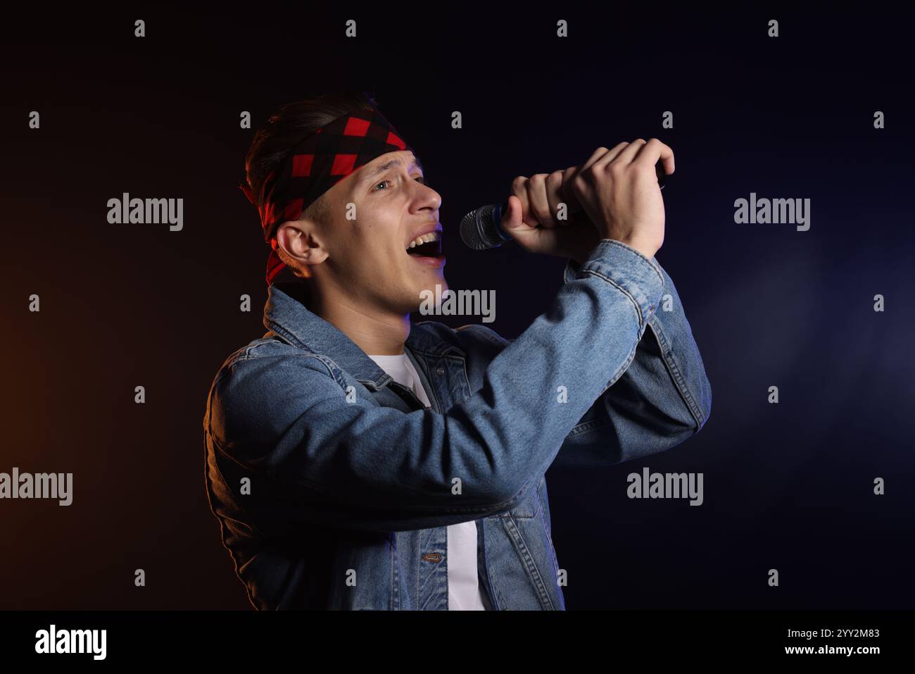 Talentierter Sänger, der auf dunklem Hintergrund mit hellem Farbton auftritt Stockfoto