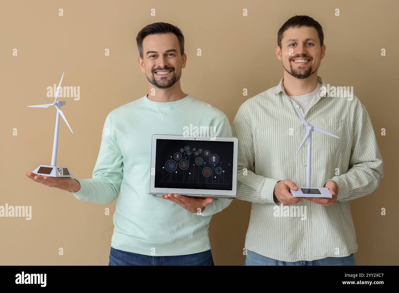 Junge Männer mit Windturbinenmodellen und Laptop auf beigefarbenem Hintergrund. Konzept der grünen Energie Stockfoto